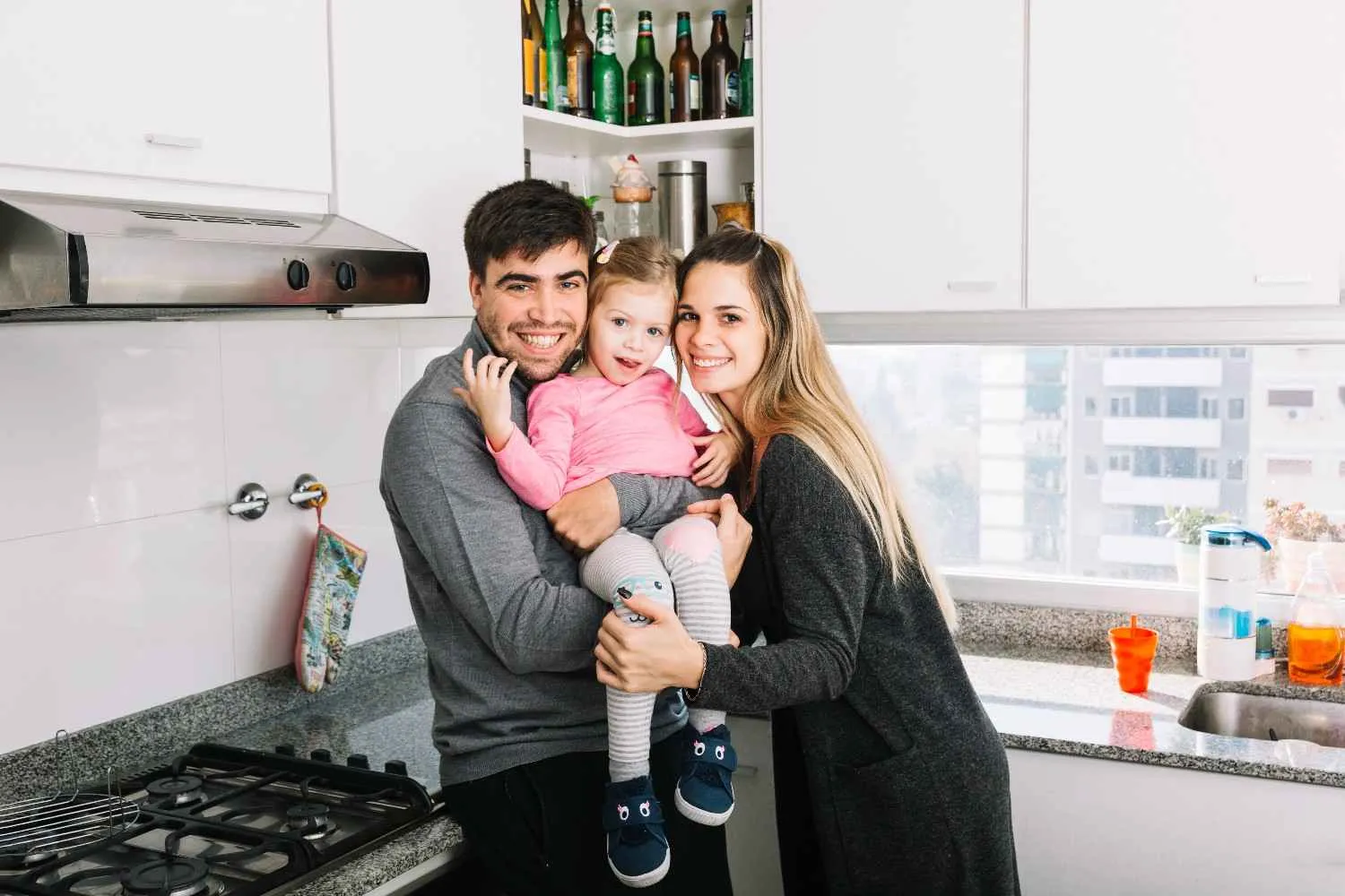 A couple holding their young daughter in the kitchen of their home