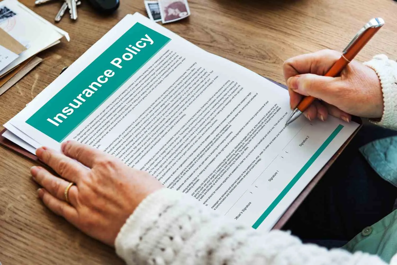 A hand signing an insurance policy document on a wooden desk