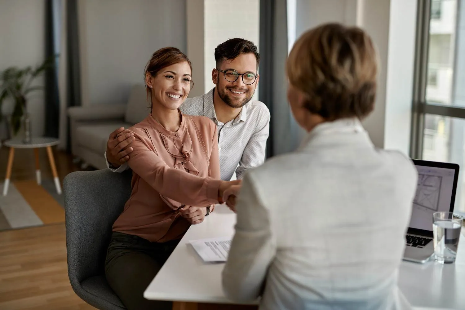 A smiling couple shaking hands across a desk